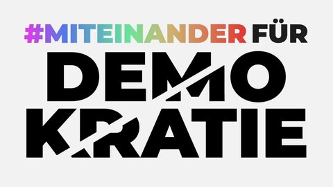 Auf dem Bild ist nur Typographie zu sehen. Zuoberst steht „#Miteinander“ in bunten Buchstaben. In schwarz folgt das Wort „für“. Darunter steht in noch größeren Buchstaben „Demokratie“. Durch das Wort verläuft ein heller Streifen, der aussieht, als würde er das Wort „Demokratie“ zerschneiden.
